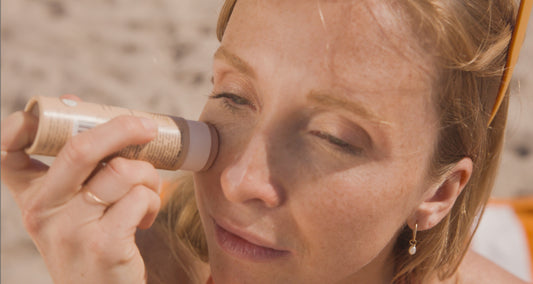 Woman applying her ATTITUDE mineral tinted sunscreen while at the beach to protect her skin after searching for sunscreen ingredients to avoid